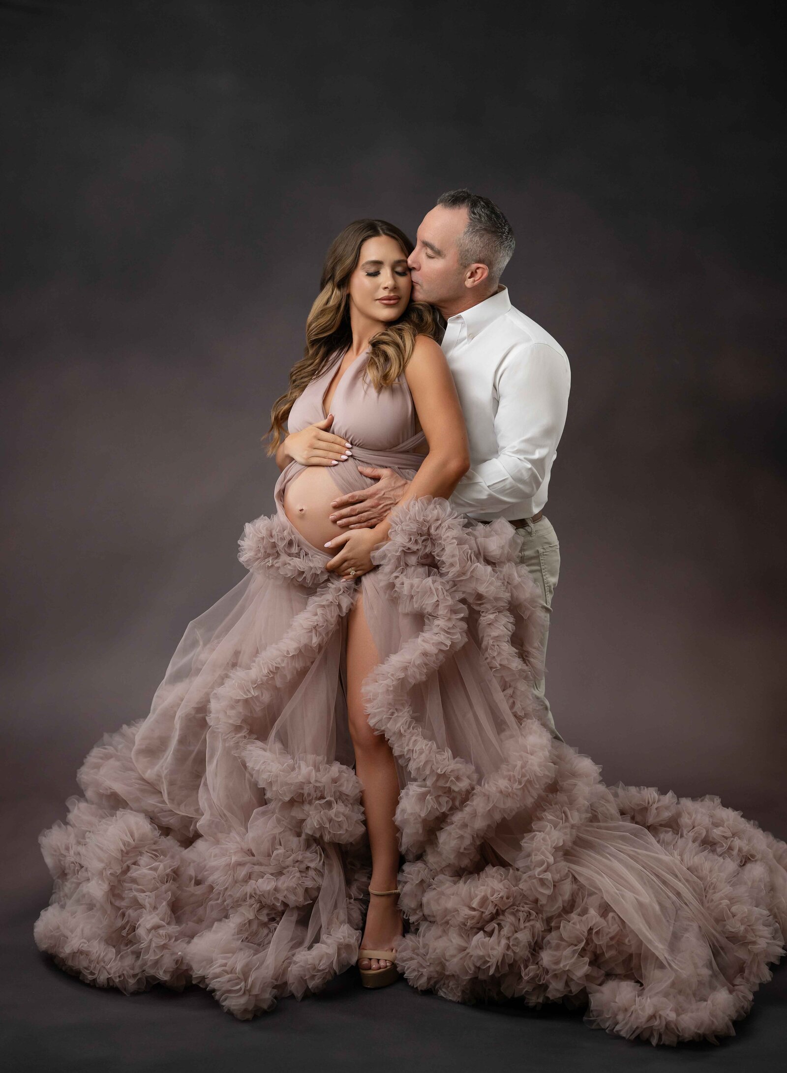 Pregnant women holding baby bump and snuggling into dad with him kissing her cheek lovingly. Photographed near Atlanta, GA
