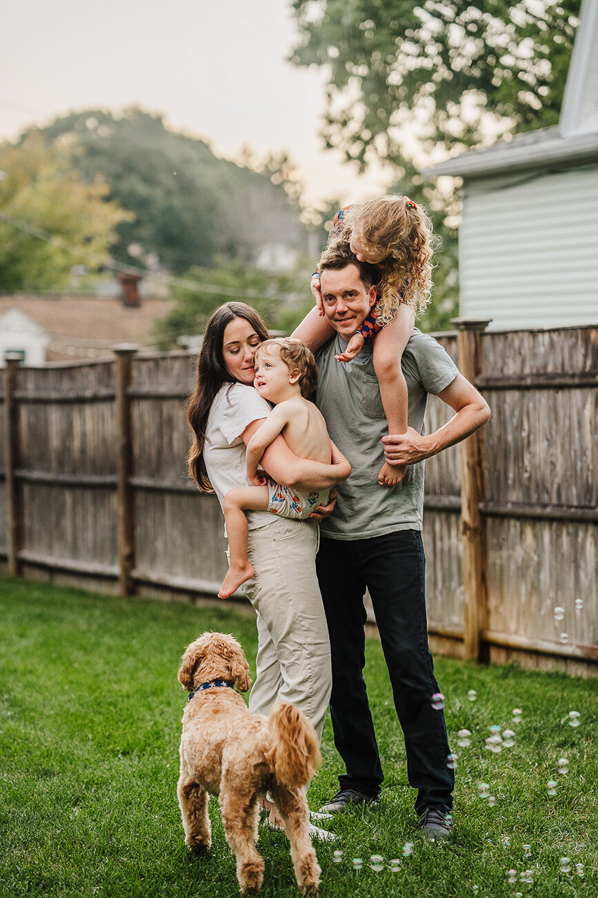family snuggles their kids and dog in fenced backyard in boston ma