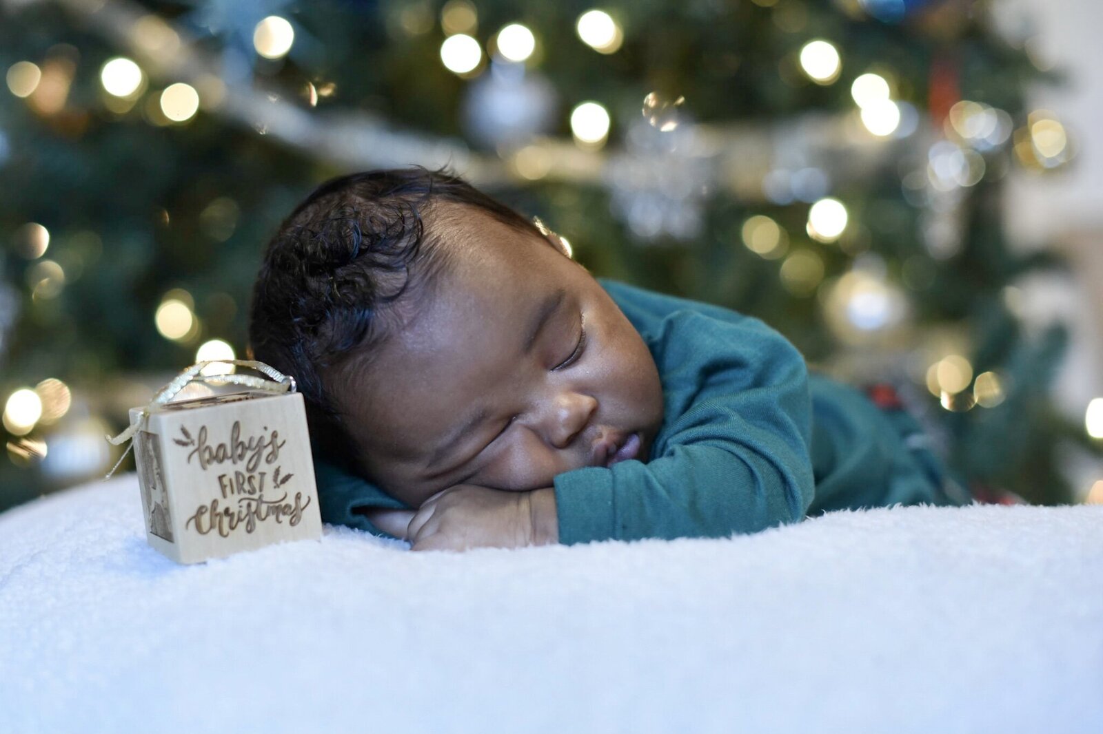 newborn baby sleeping under the christmas tree with an ornament that reads babys first christmas photographed by Millz Photography in Greenville, SC