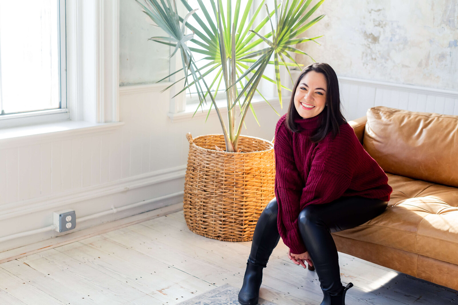 brunette woman wearing burgundy sweater sitting on couch in front of plant