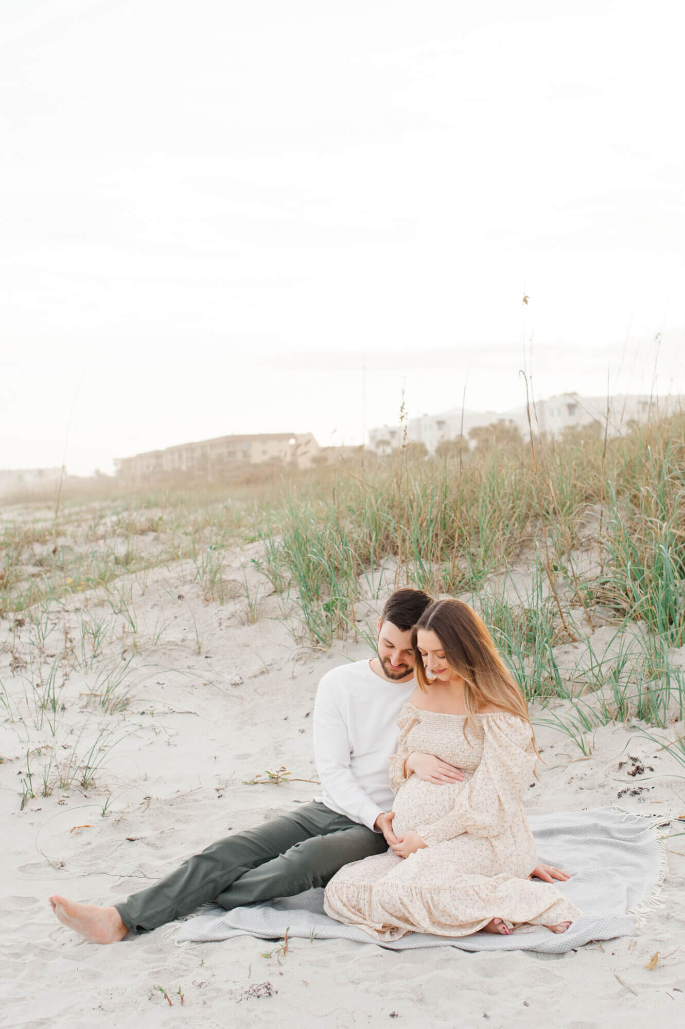 Orlando maternity session on the beach of mom and dad sitting in the dunes holding her belly
