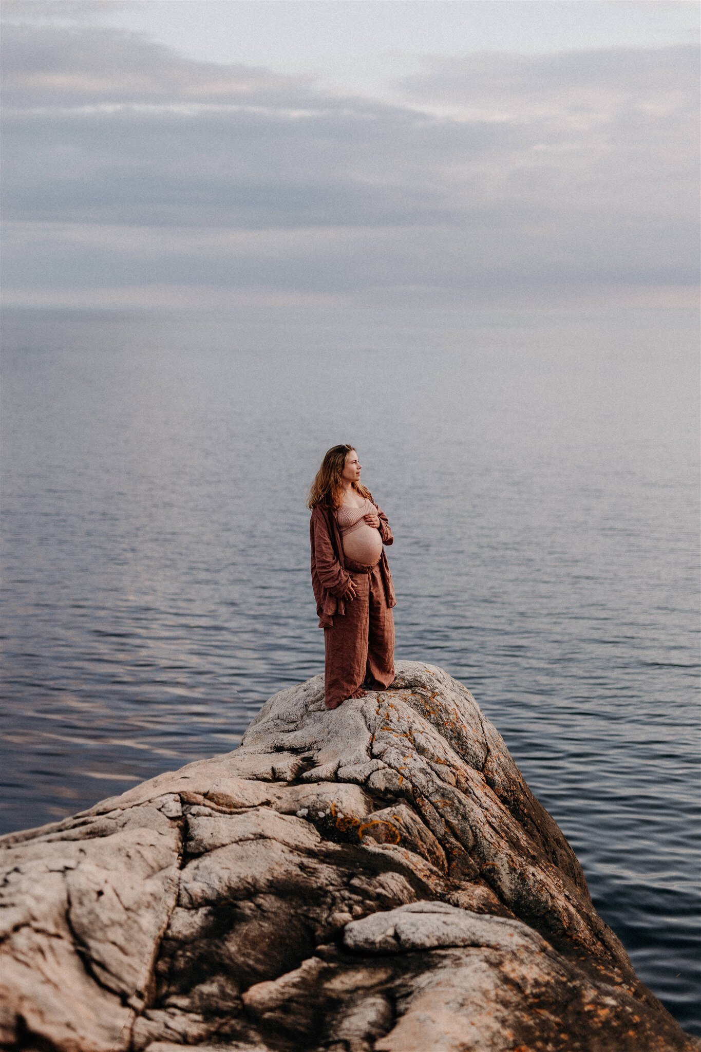 en gravid mamma står i ett matchande linneset och blickar ut över havet