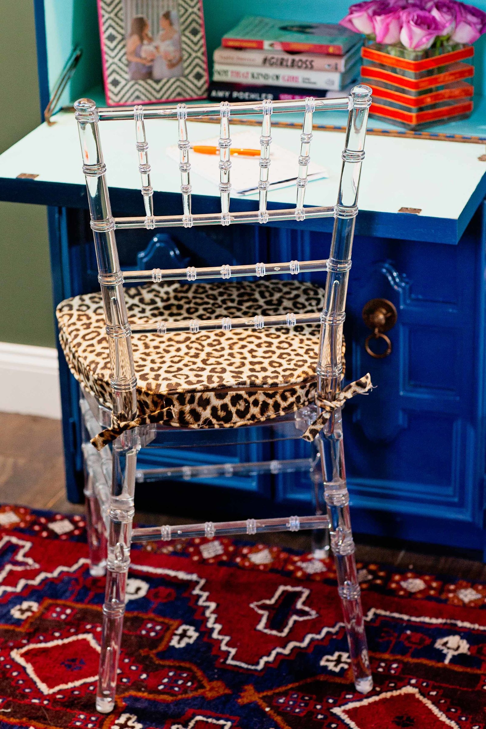 A blue writing desk with a clear acrylic chair and leopard print cushion.