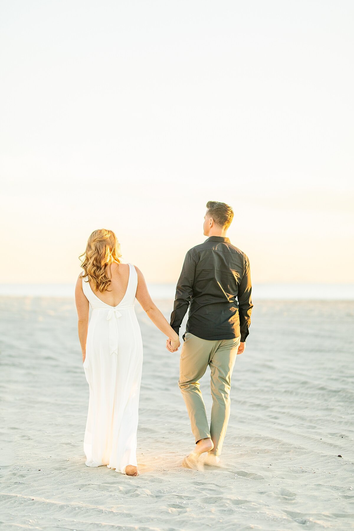 Couple holding hands walking towards the ocean together while dolphins play.