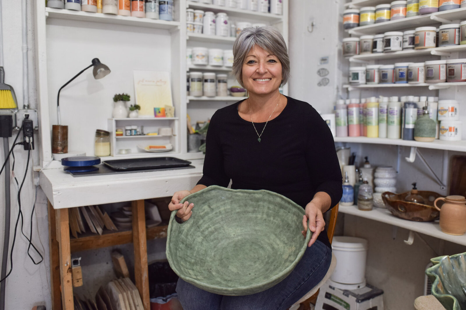 Jill sits in her Key West, FL and Laingsburg, MI studio holding a large green serving dish with handles