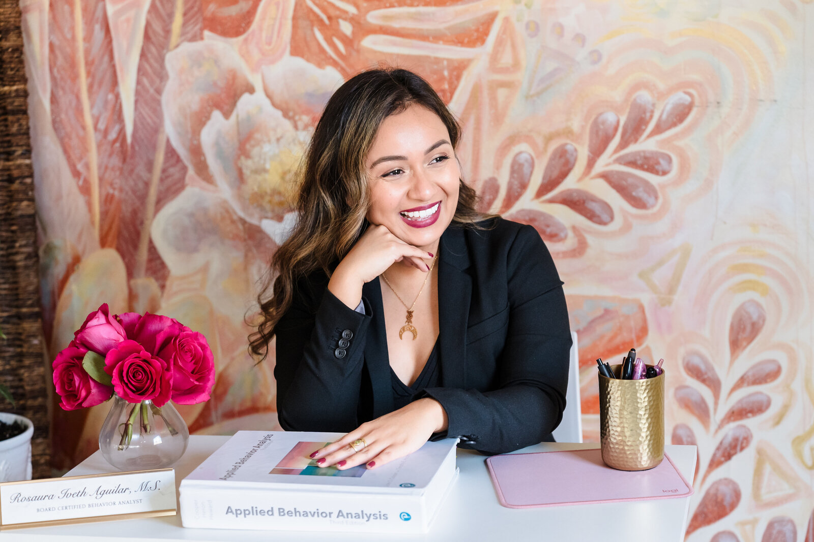 Life coach sits in her desk and one of her hands in her chin, and smiles