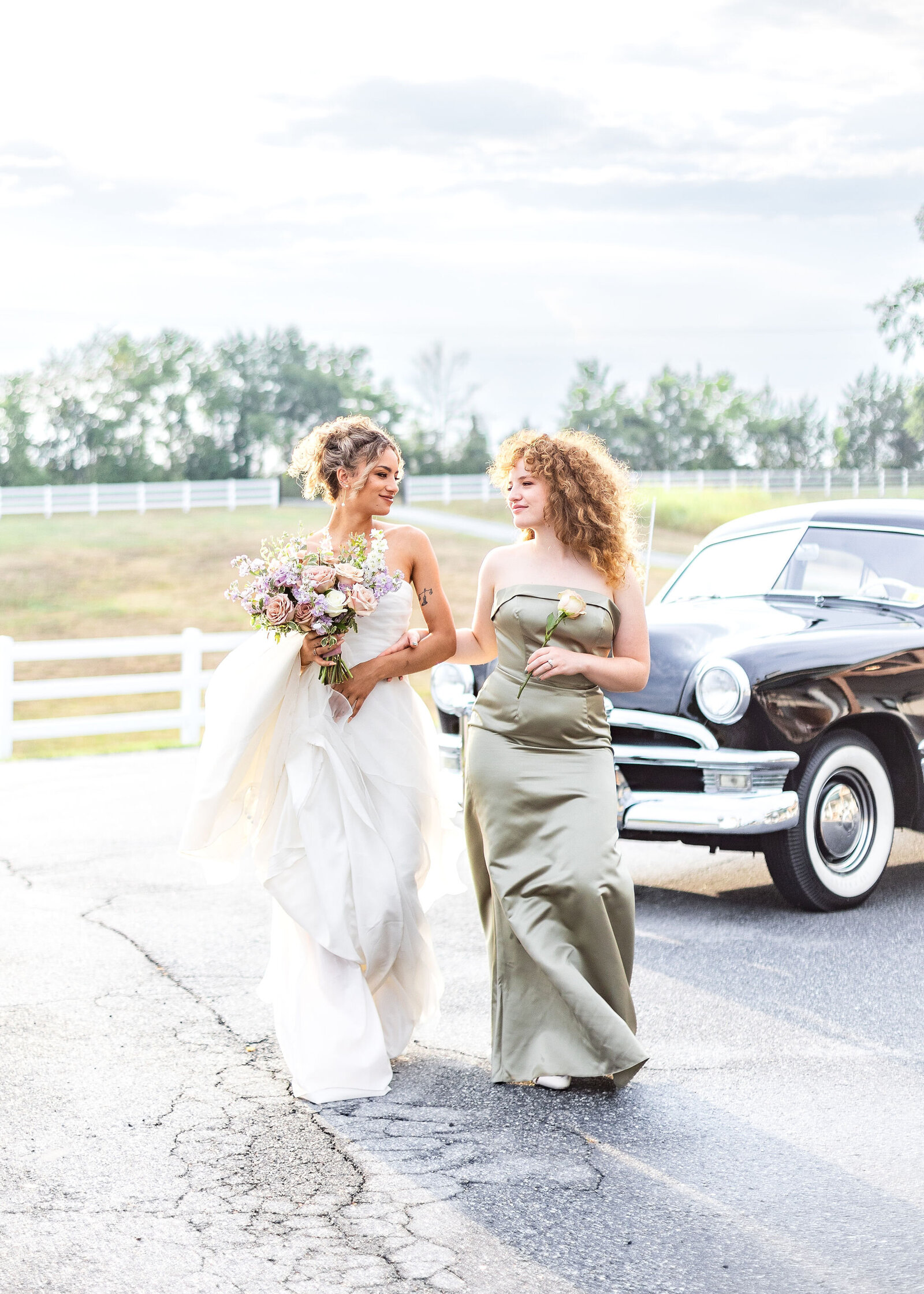 Bride and bridesmaid posing beside a vintage car at Willow and Stone Events in Mocksville, NC, perfect for classic countryside weddings.
