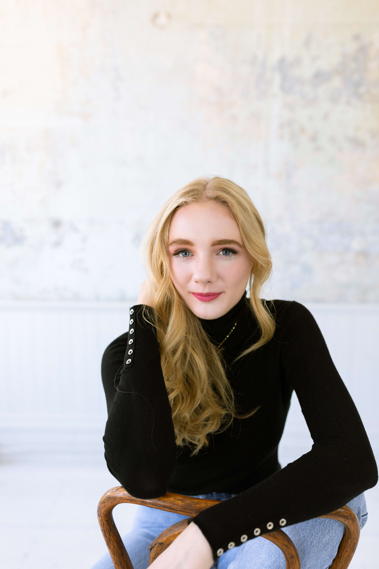 blonde girl with red lipstick wearing a black turtleneck and blue jeans posing for senior pictures