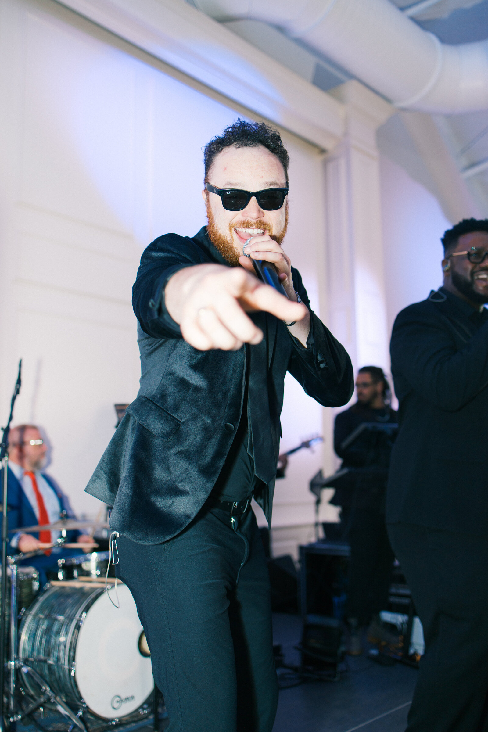 singer with black sunglassss and mic in hand singing points at camera at wedding reception