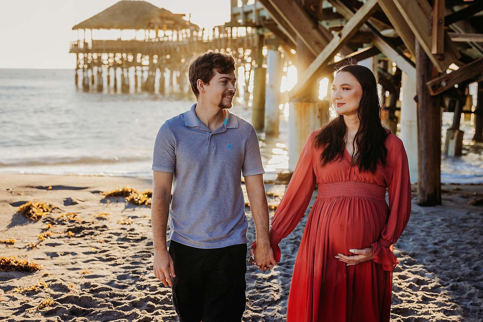 couple holding hands durimg a sunrise maternity photo session in Cocoa beach, Florida.