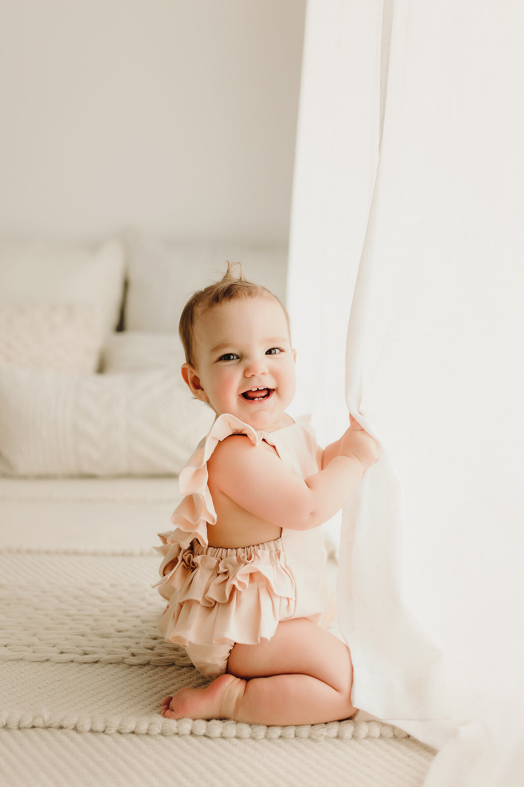 A 9 month old baby girl sits playing for a picture during her photoshoot inside a Vancouver Washington natural light studio