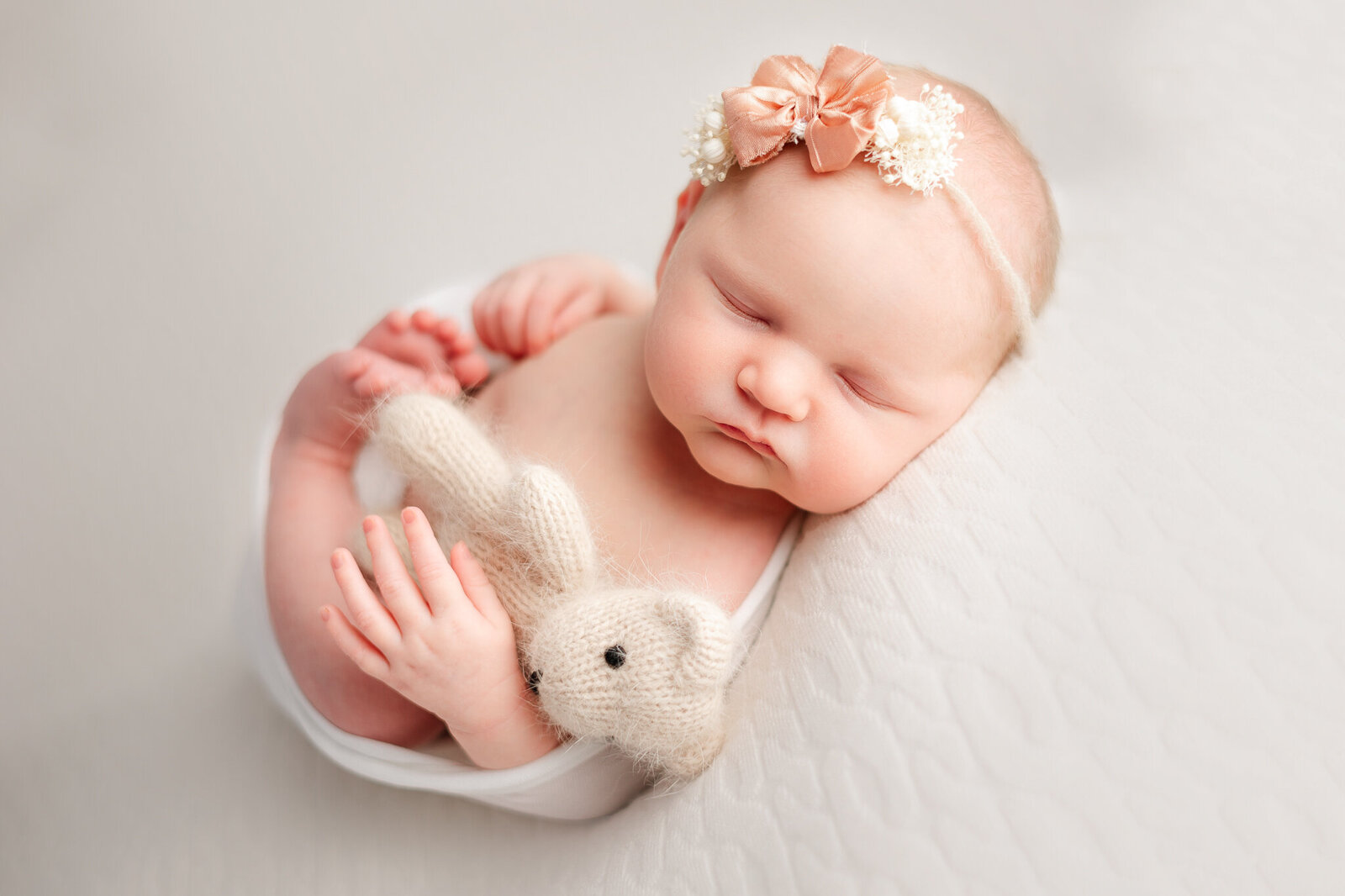 Newborn girl wearing pink bow holding a tiny teddy bear