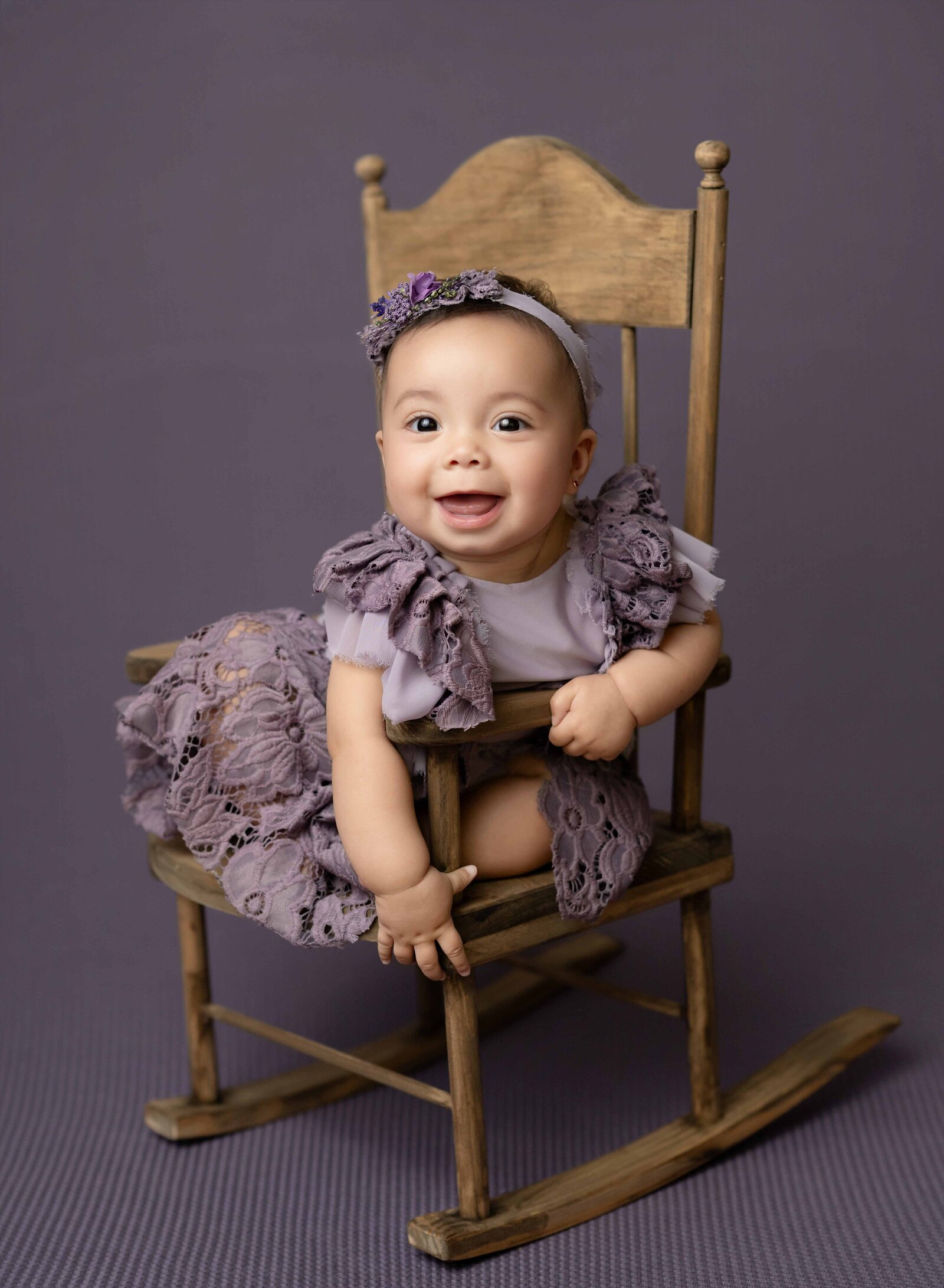 Baby girl sitting in wooden rocking chair and smiling.