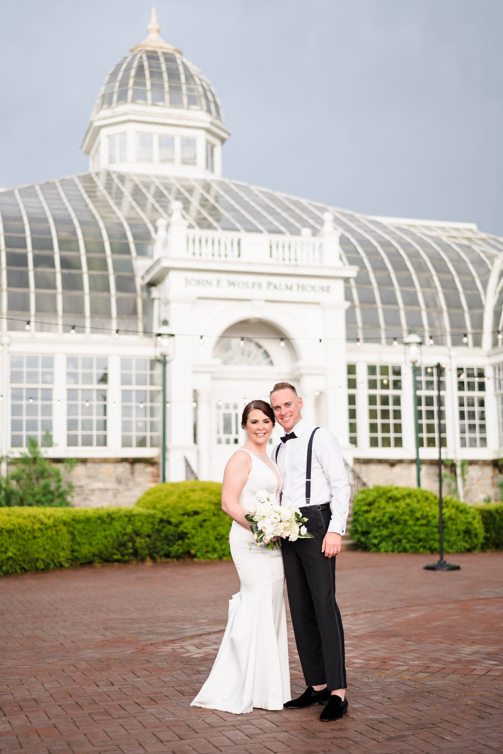 Bride and groom hold each other and smile in front of the Palm House at the Franklin Park Conservatory