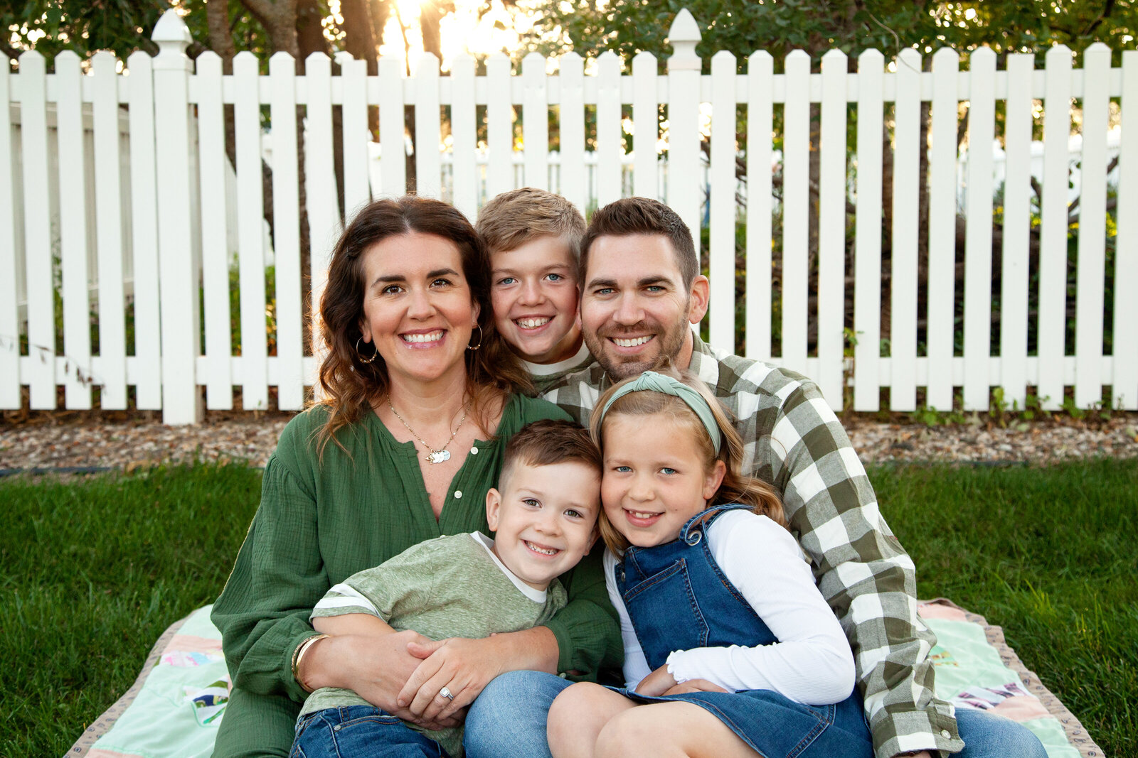 Family of five snuggled close together on blanket, smiling.