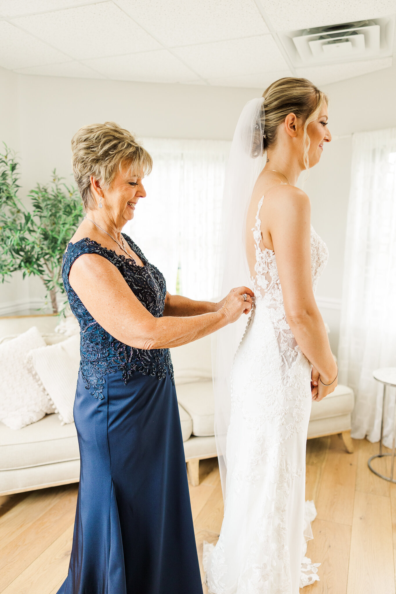 Candid moment of bride’s mother fastening the back of the wedding gown at SkyView Golf Club