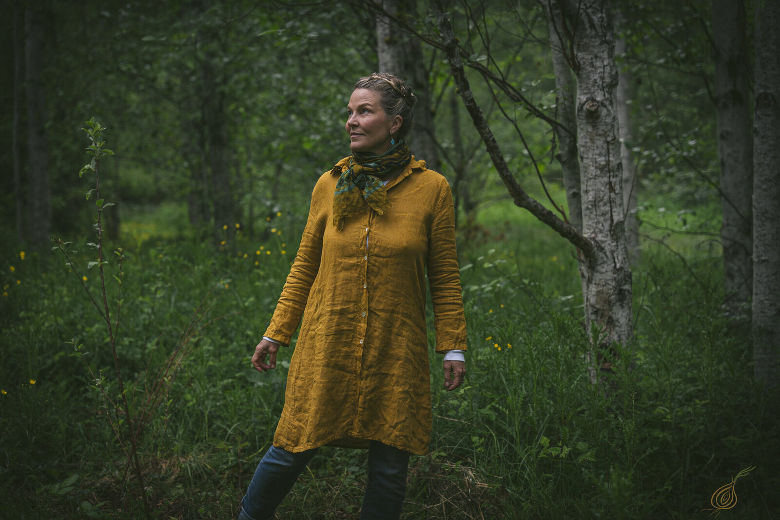A woman wearing a bright yellow dress poses in a forest, surrounded by trees and the peaceful ambiance of the outdoors.