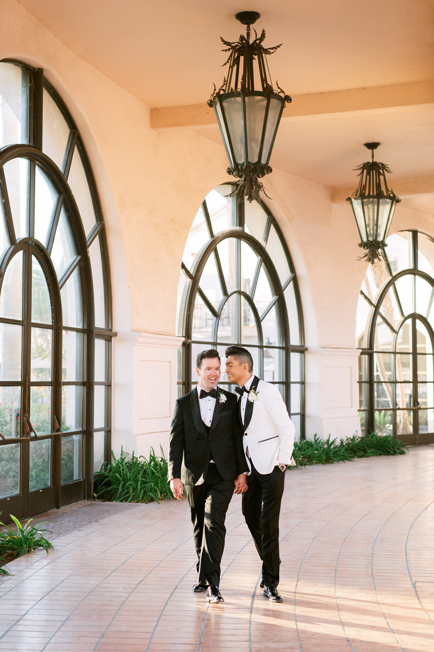 Gay couple walk down a windowed hallway on their wedding day