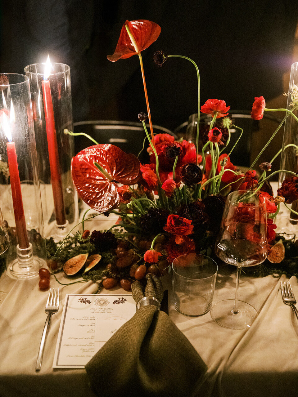 Elegant tablescape with rich red floral arrangements, taper candles, and deep-toned decor for a dramatic atmosphere.