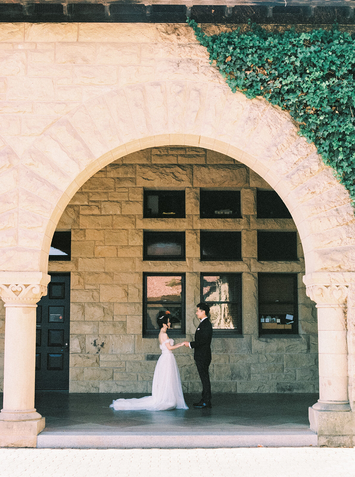 The bride and groom share a romantic moment under the iconic arches of Stanford University, capturing the essence of their love.