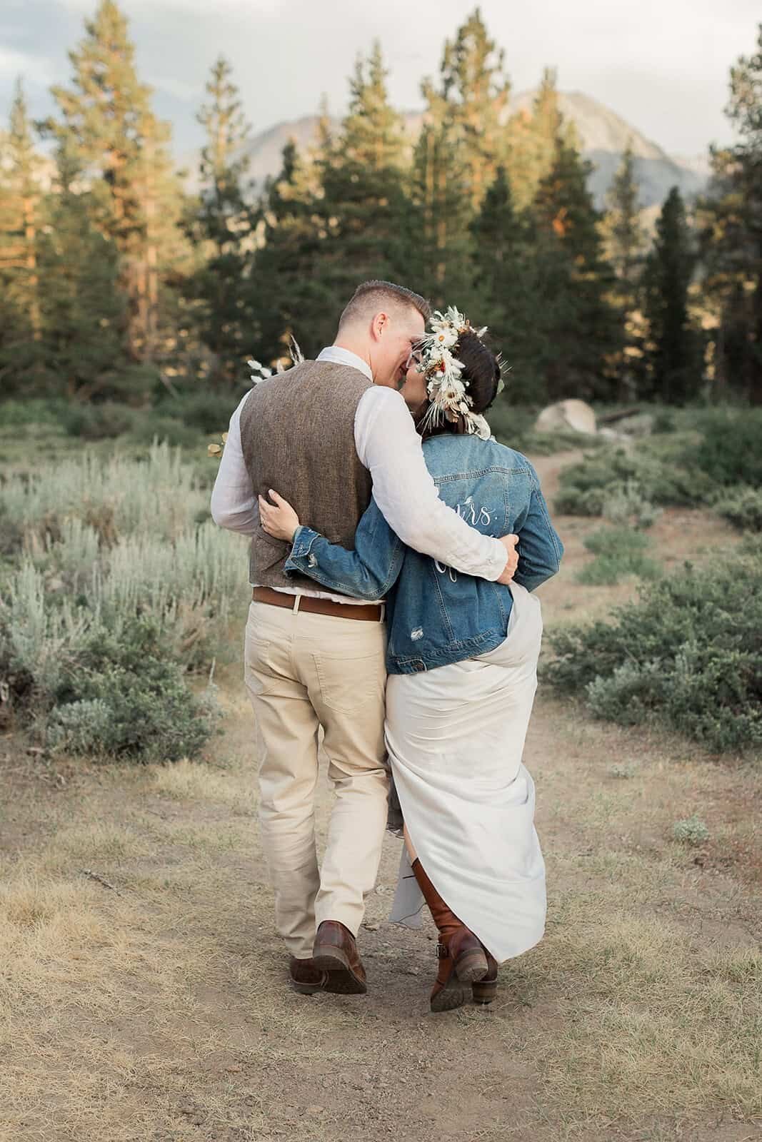 A bride and groom walk down a dirt path surrounded by pine trees on their Mammoth Wedding day. 