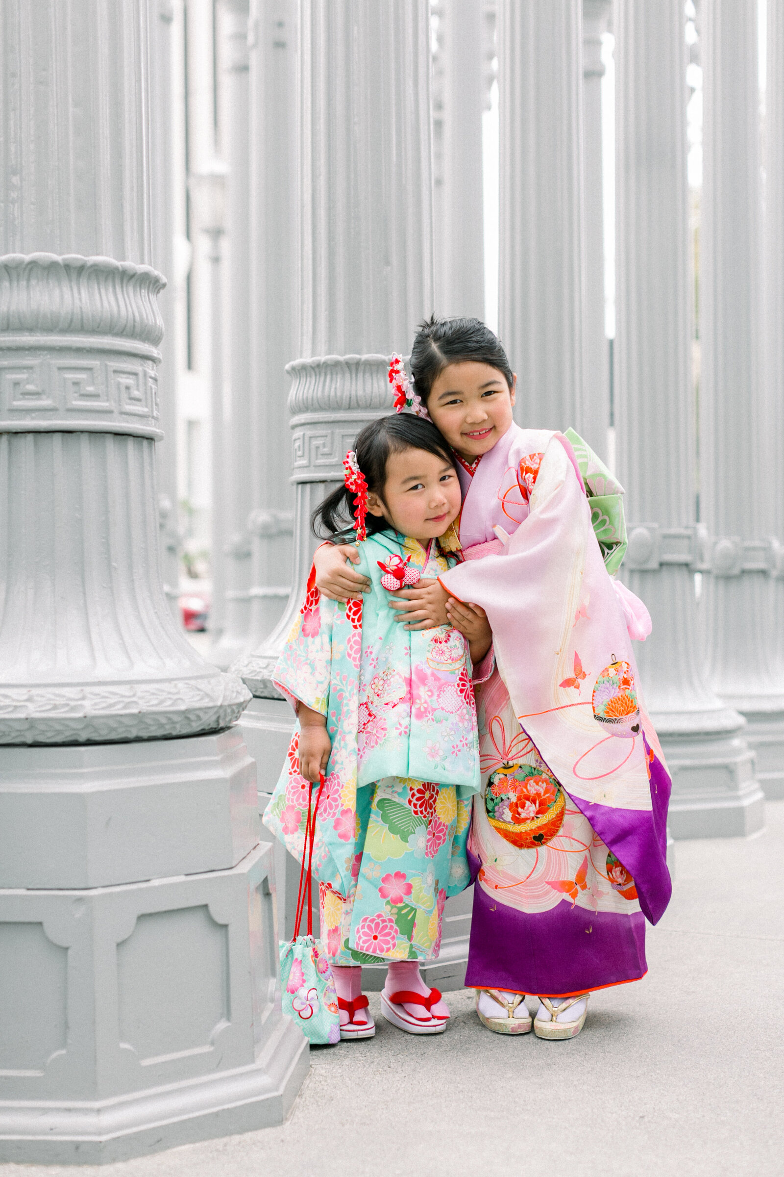 Two sisters in colorful kimono hugging at Urban Light installation | ロサンゼルス アーバンライト 七五三 姉妹着物記念