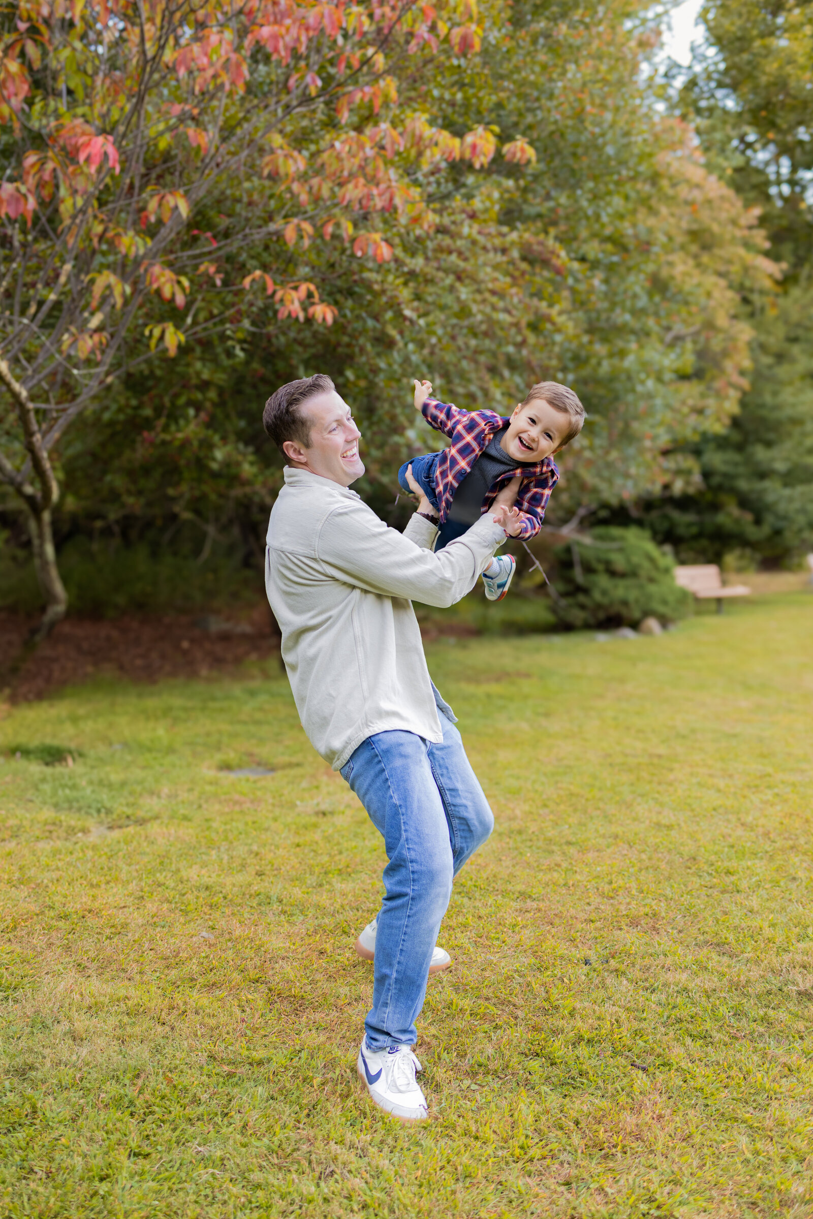 Father playing airplane with his son while both of them laugh during and outdoor family session in Northern New Jersey