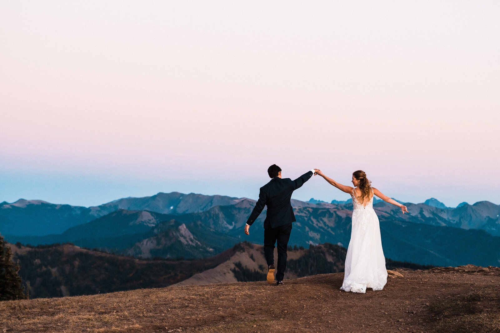 a groom leads his bride towards the olympic mountains at twilight