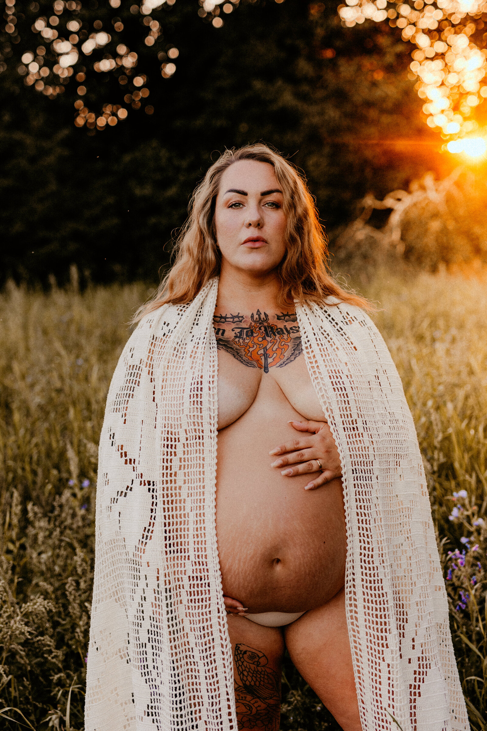 en plus size gravid mamma håller om sin mage på ett blomfält