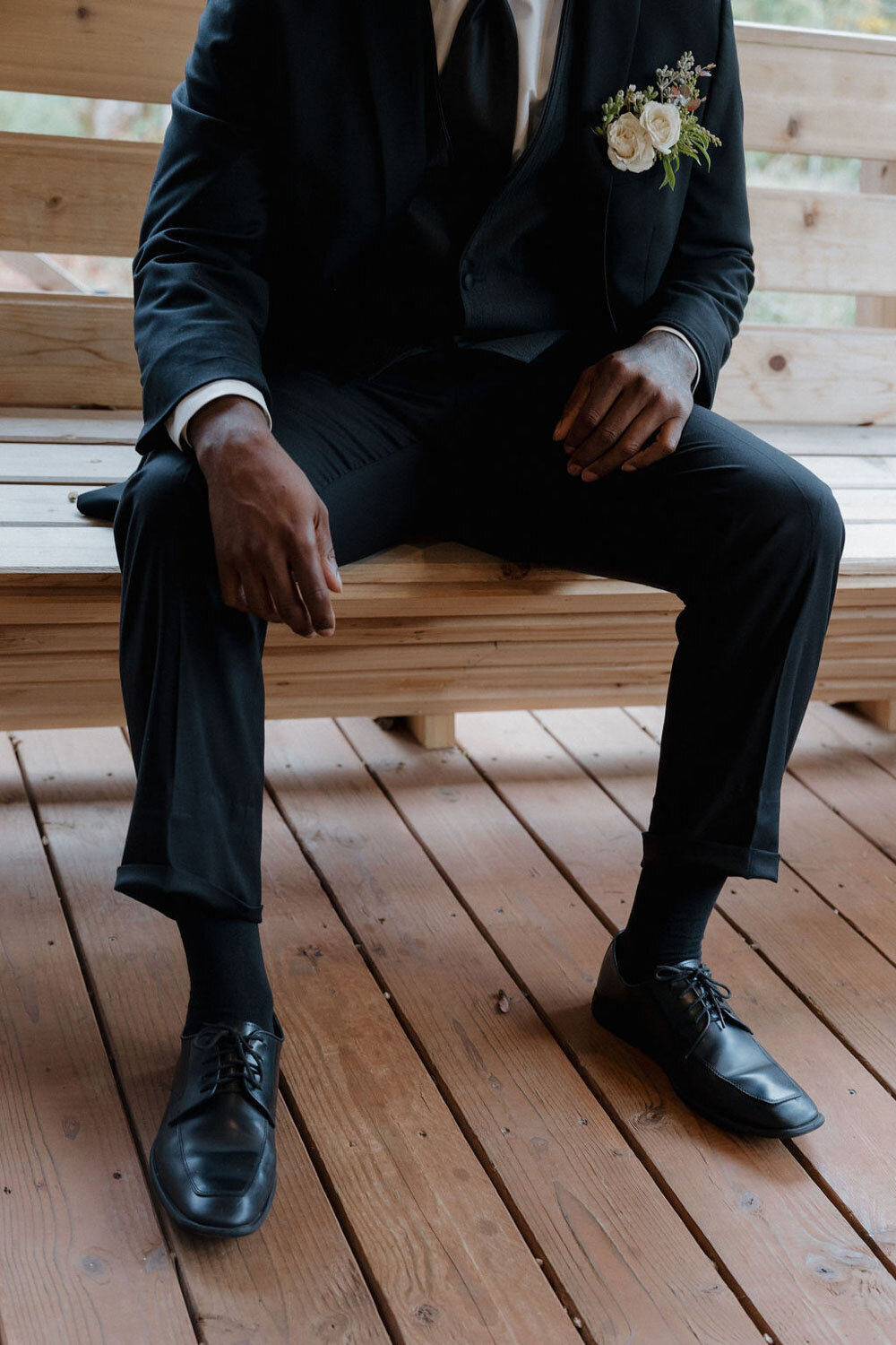 Groom in black suit sitting on a wooden bench