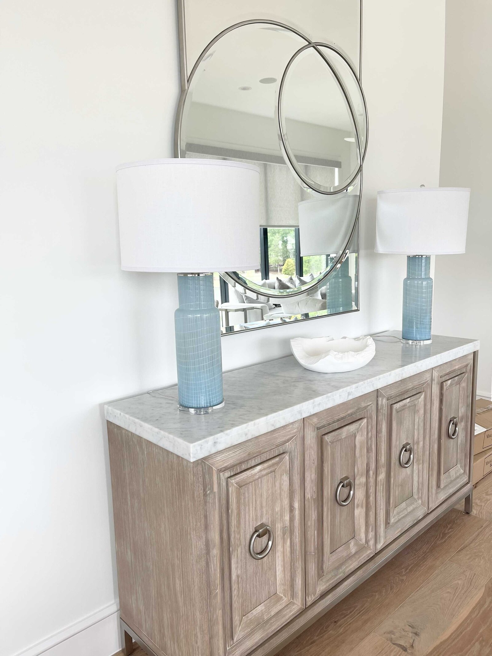 Renovation and interior design in Frisco, featuring a large wood table with elegant lamps overhead, a big circular mirror on the wall, and sophisticated lighting elements.