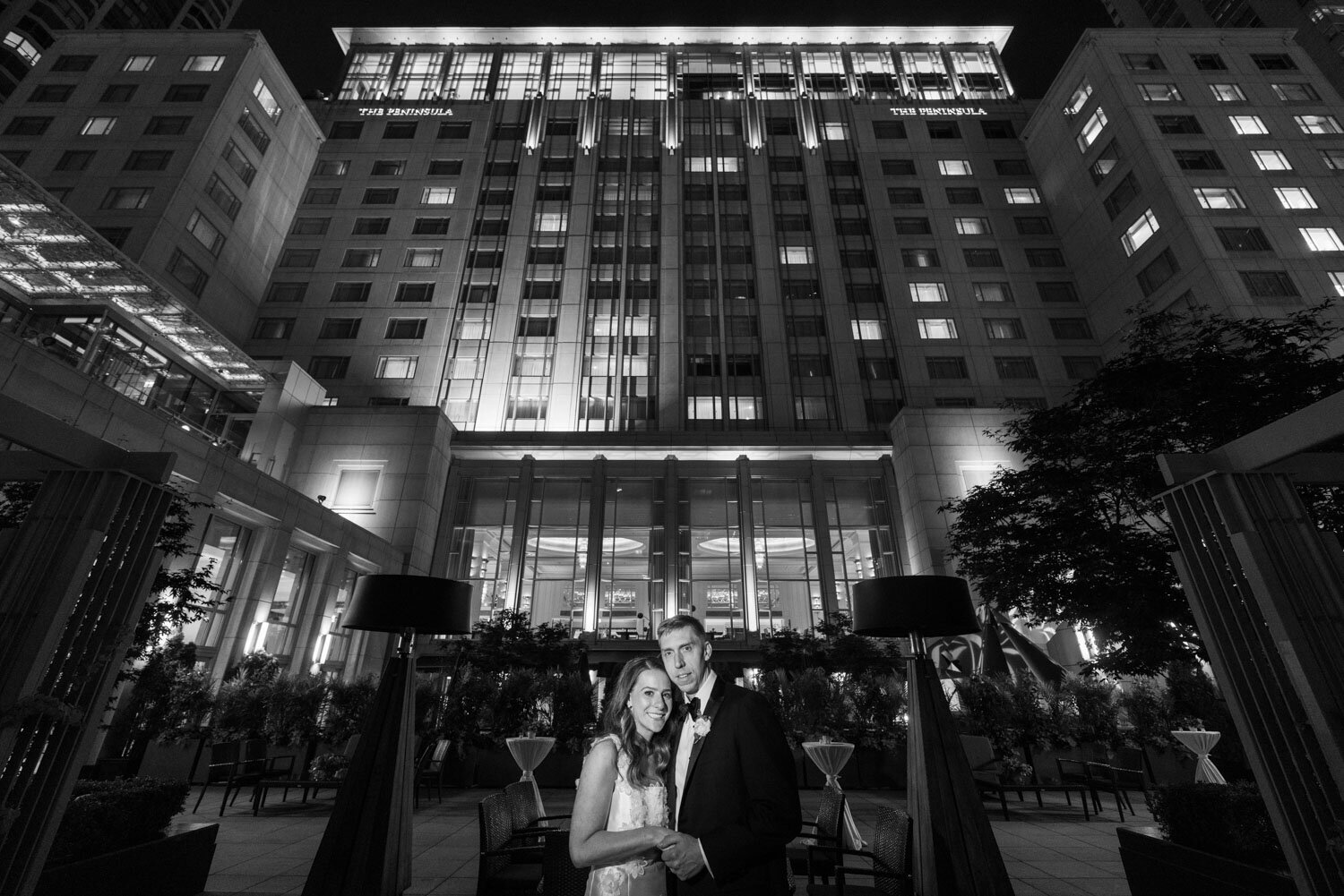 A black and white photo of a bride and groom in front of a large building