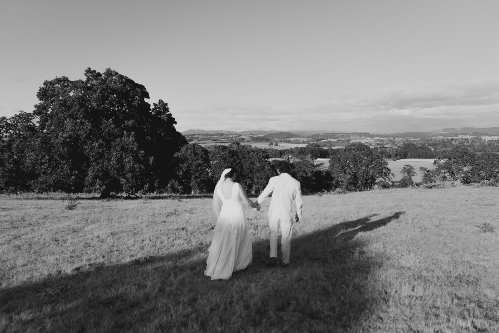 Bride and groom walk away from camera in a field