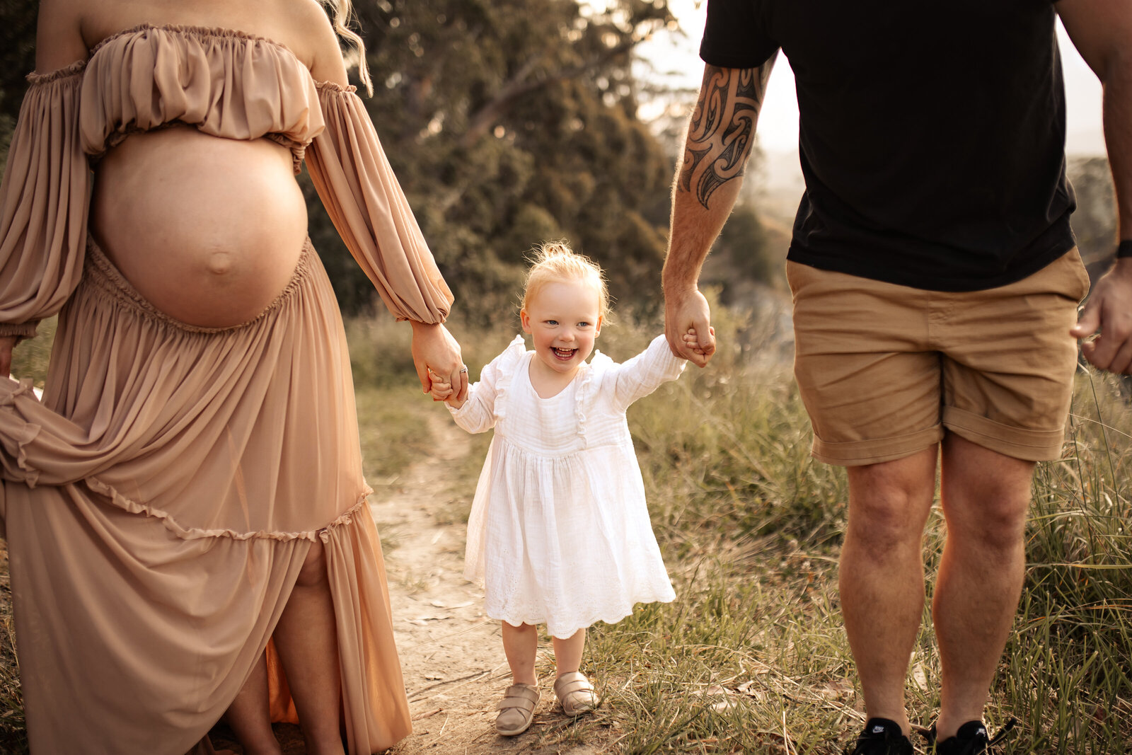Toddler laughing while swinging between parents at Te Mata Peak during a golden hour family session – candid Hawke’s Bay photographer with scenic views