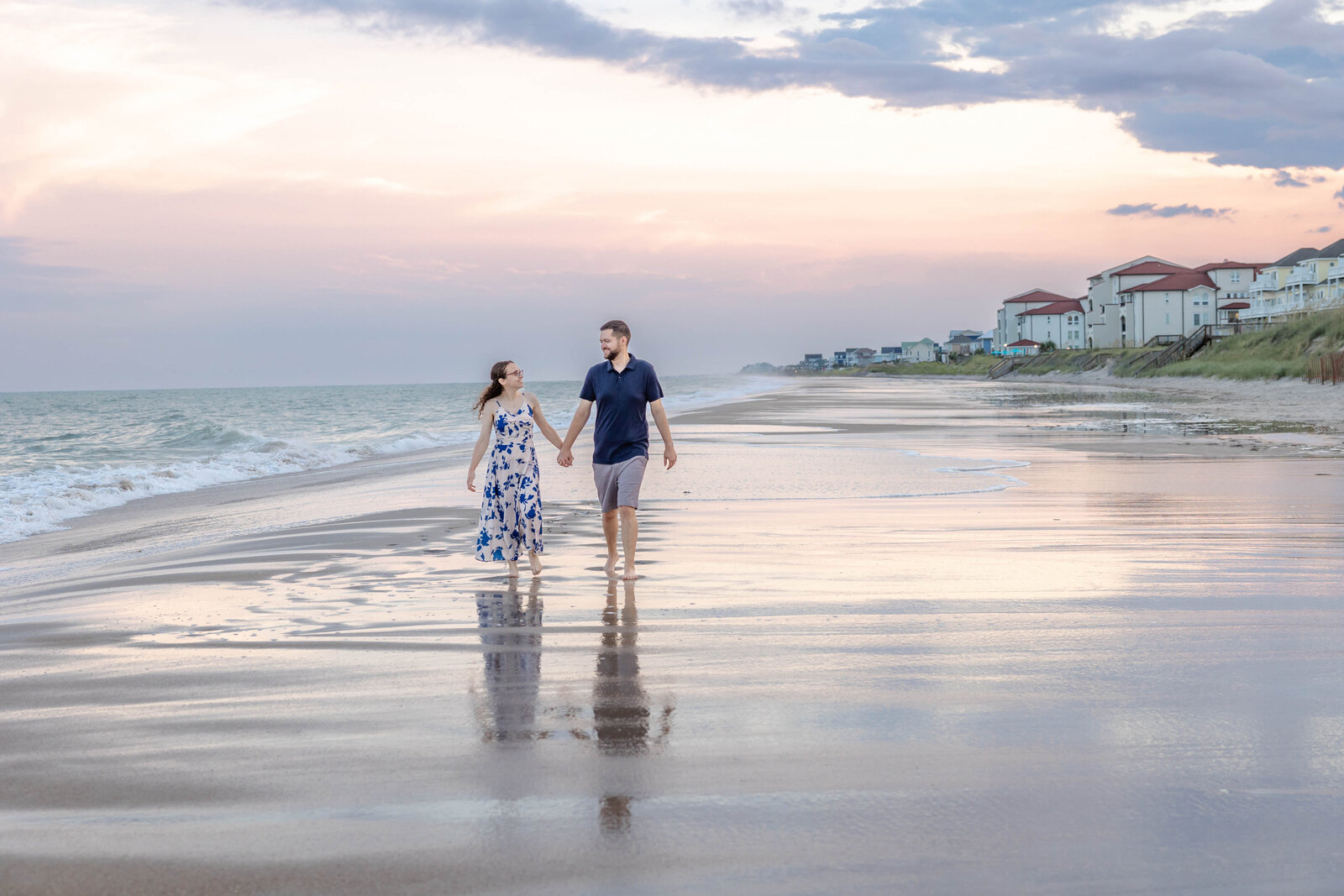 A couple walking hand-in-hand along the shoreline in North Topsail Beach, NC, during a stunning sunset. This romantic image highlights the beauty of candid wedding photography, perfect for those looking for professional wedding photography in North Carolina.
