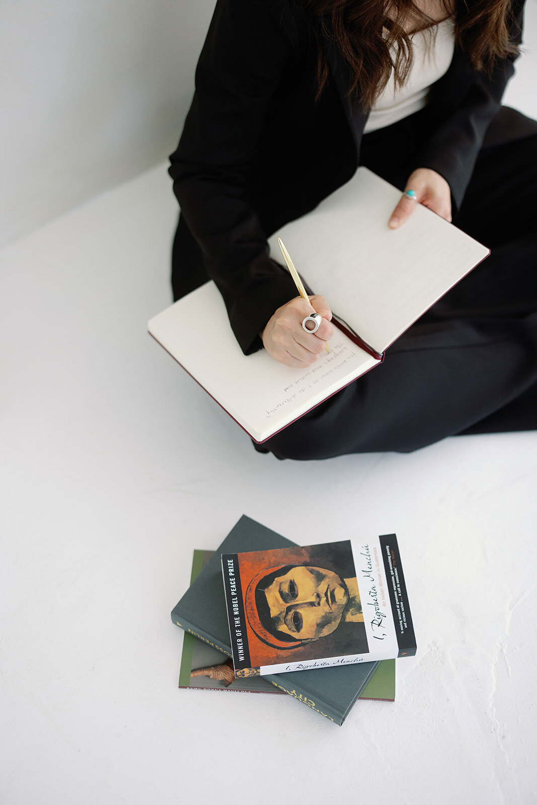 Close-up of a woman writing in a journal with books stacked nearby, symbolizing creativity and professionalism.