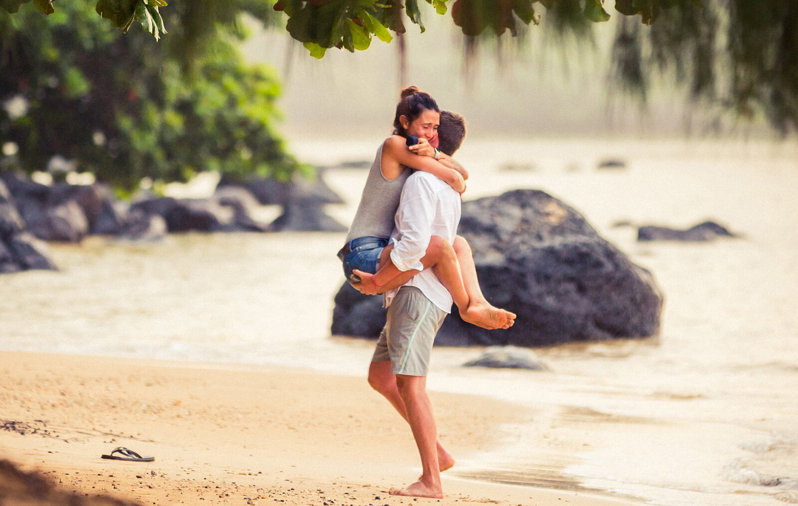 Happy emotional girl jumping up, with legs rapped around him, up on her future husband to be at their surprise proposal engagement in Oahu