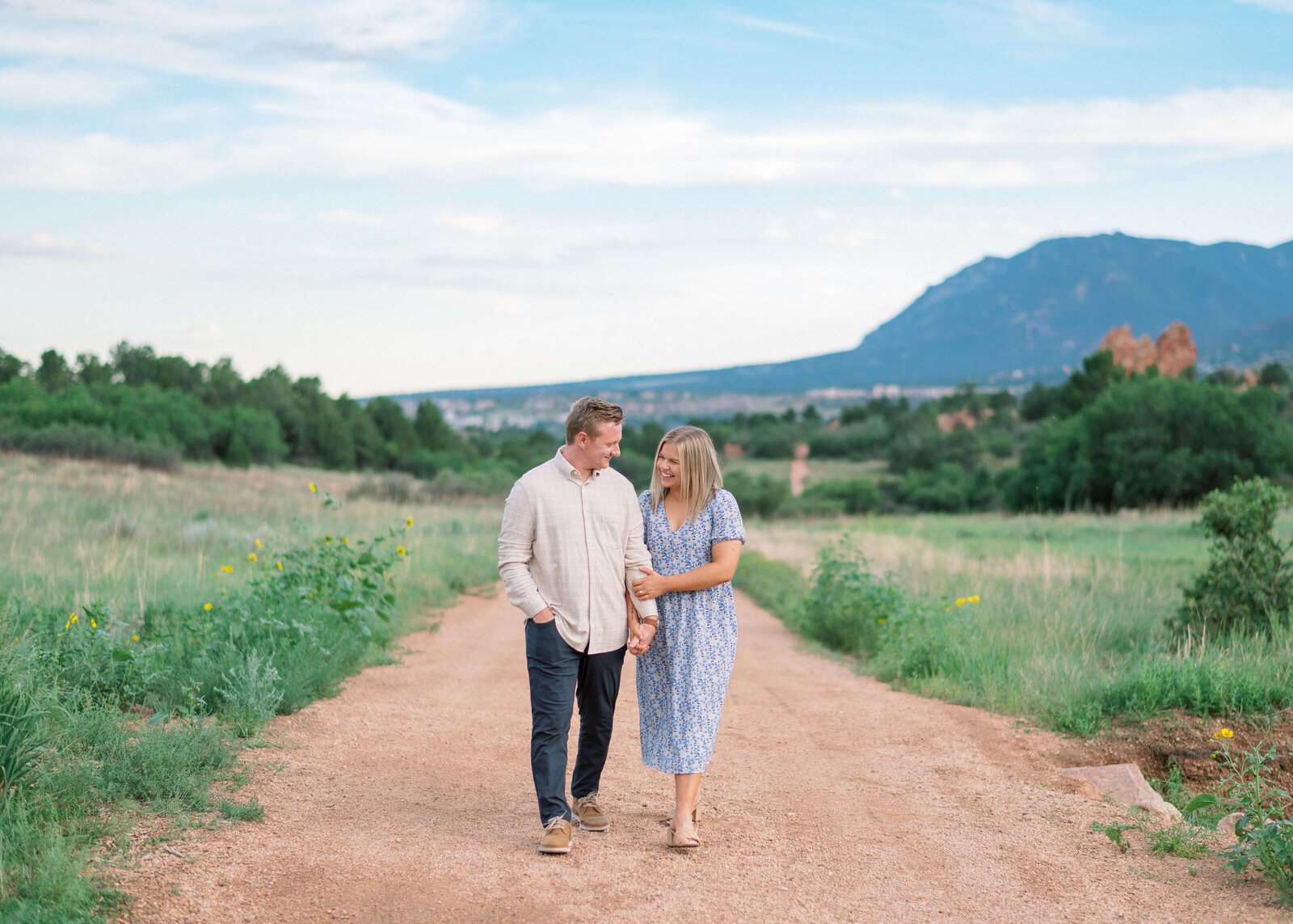 A couple links arms and walks down a dirt path together during their engagement session with virginia wedding photographer