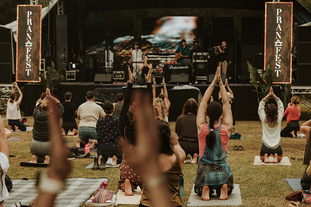 Group practicing yoga and raising hands at an outdoor music and wellness festival, captured by event photographer Sunshine Coast.