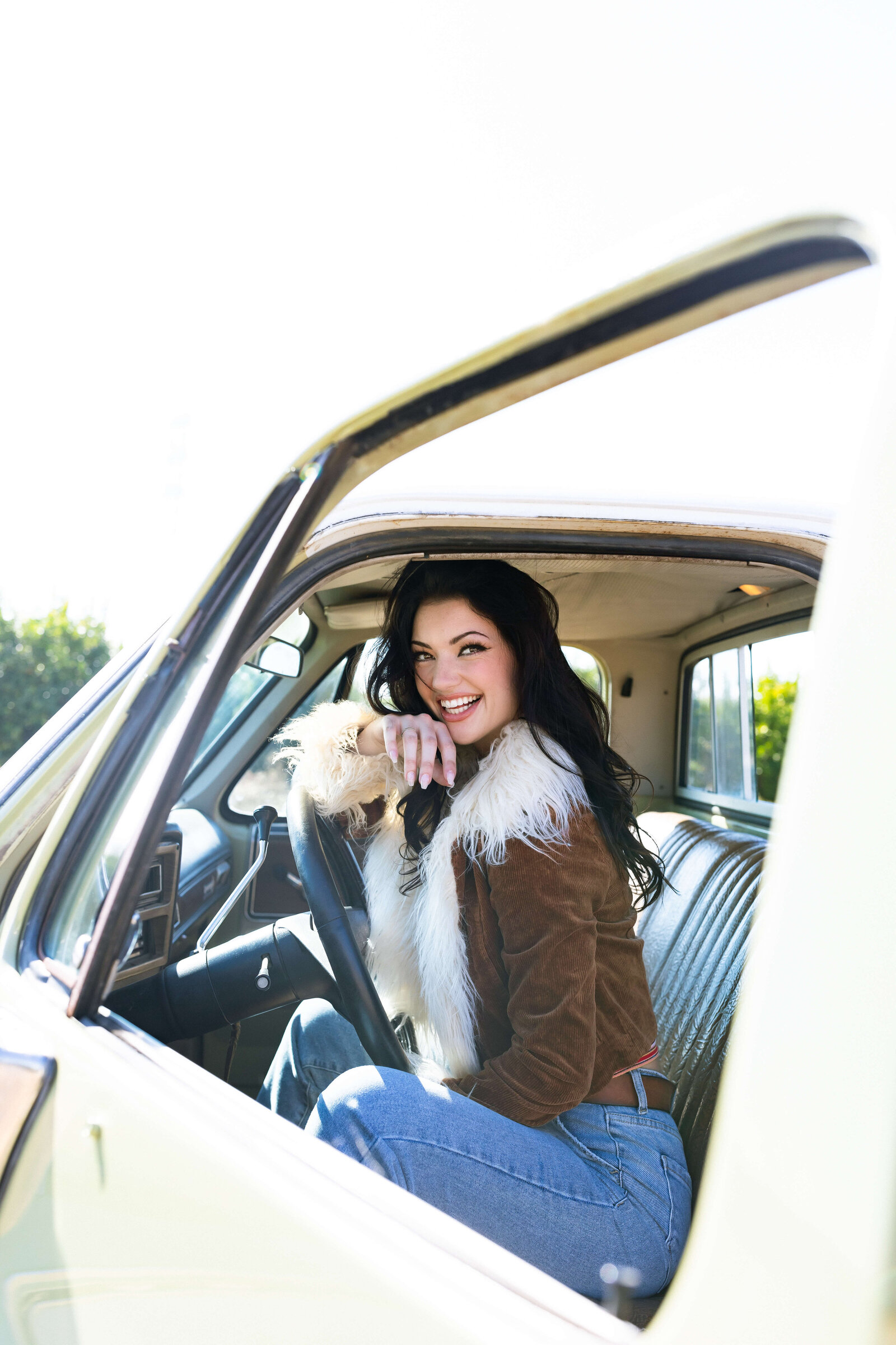 dark haired girl wearing fur coat smiling and sitting in an old green truck