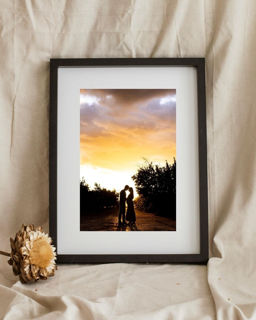 Matted black frame that features an image of an expecting couples silhouette against a pink sunset. 