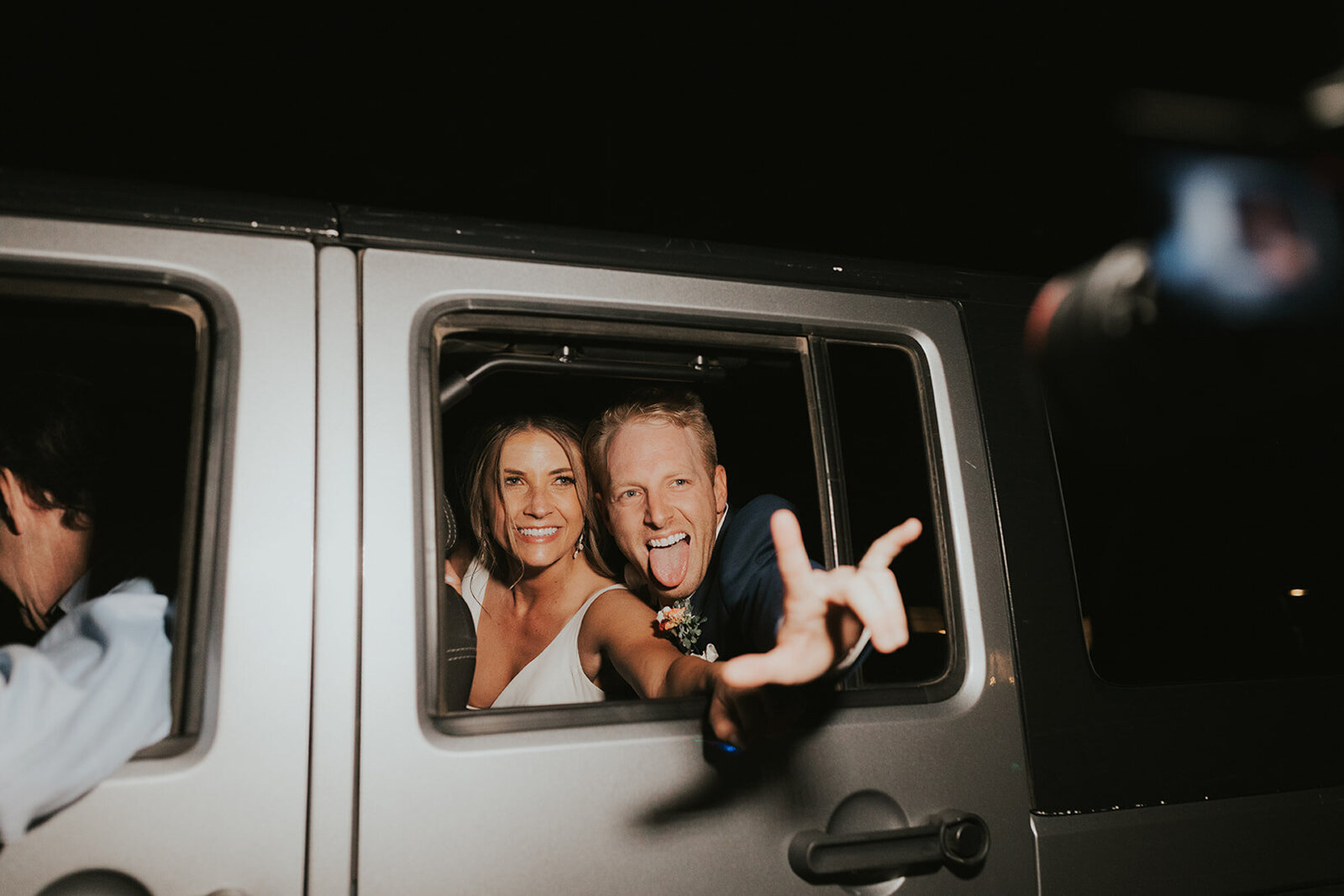 Bride and groom riding their getaway car saying goodbye to their guests