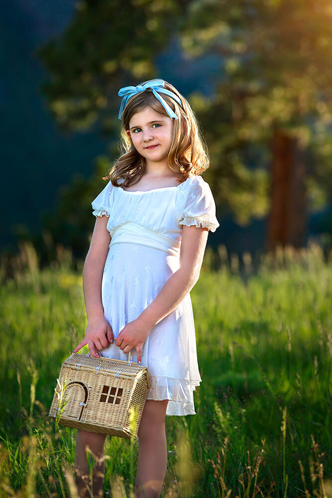 beautiful-young-girl-kid-child-white-dress-blue-hair-ribbons-timeless-mountain-background-holding-toy-flower-house-vibrant-colors-fine-art-family-children-colorado-photographer