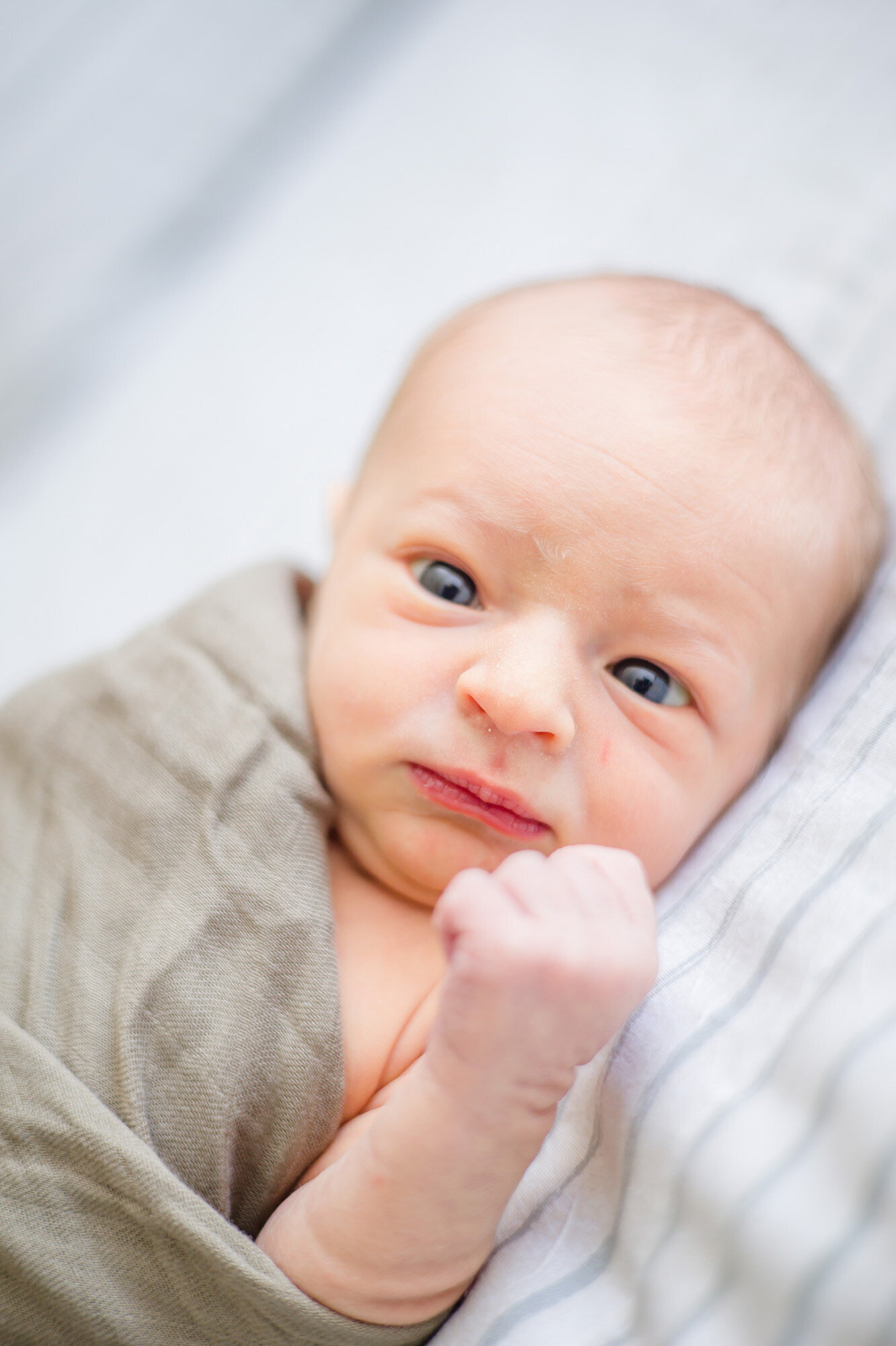 Newborn baby boy awake on a bed wrapped in a green swaddle