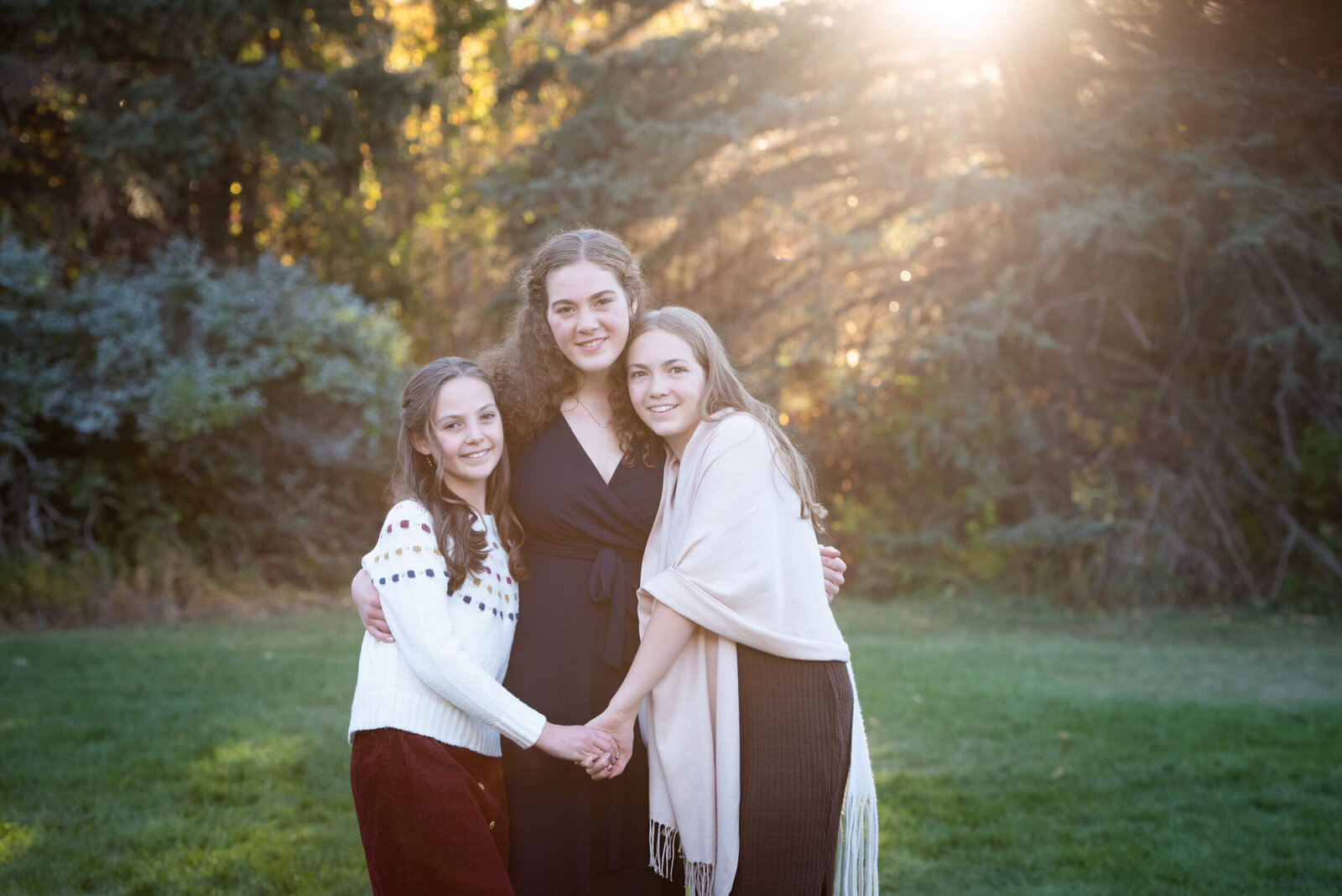 Mom hugging her daughters in a park field at sunset