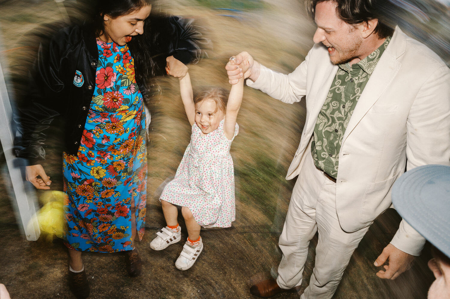Young wedding guest is lifted up by her parents.