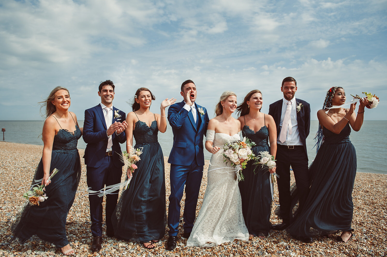 Bridal party celebrate and make noise as they stand for a group shot on the beach in Deal Kent