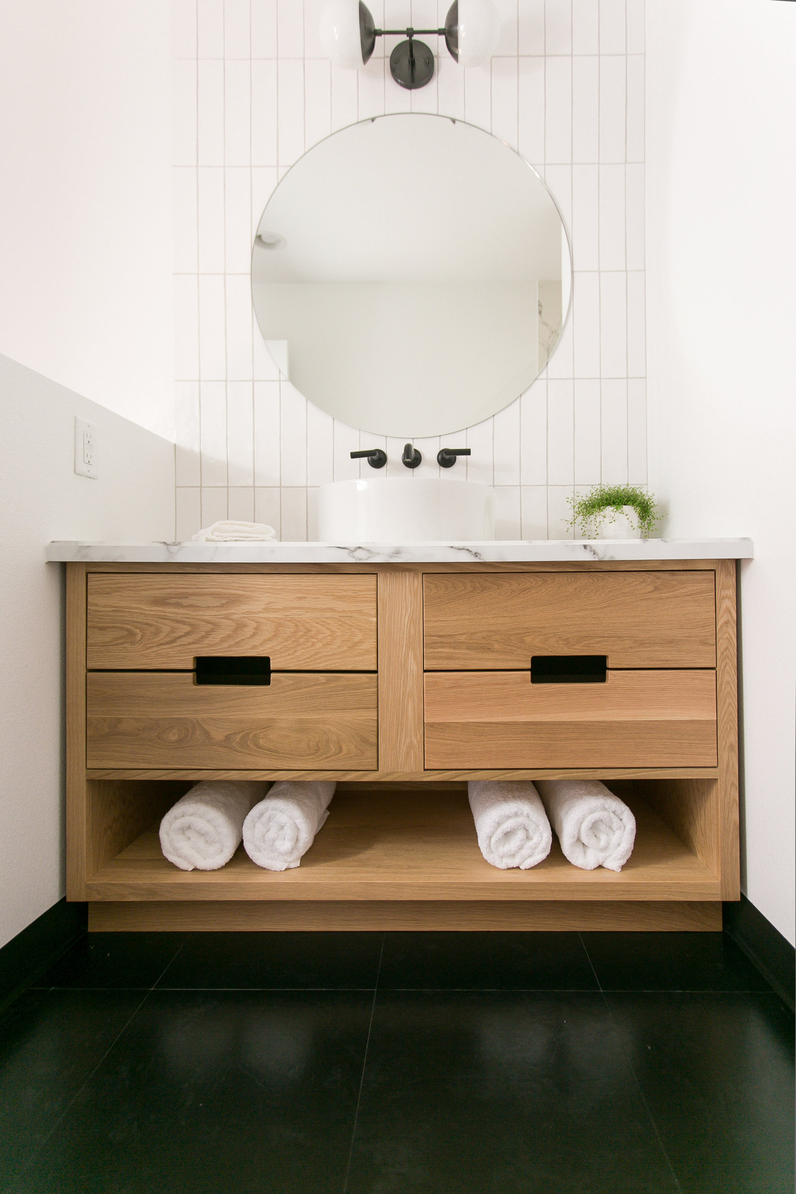 Modern BnB Bath with custom mid tone vanity. The straight stack vertical tile frames the modern vessel sink design with a wall mounted faucet marble patterned countertop.