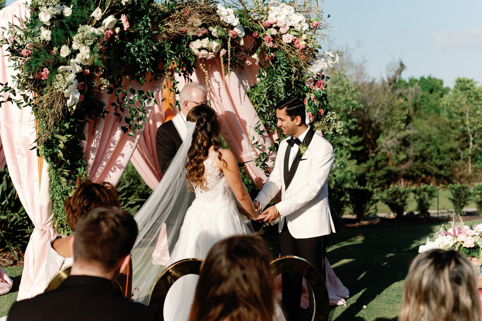 bride and groom standing at their altar. They are looking toward their officiant and their guests can be seen in the foreground