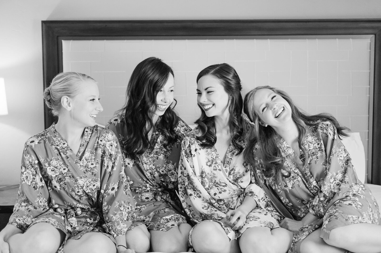 Bride with bridesmaids laughing on the bed at the Wigwam.